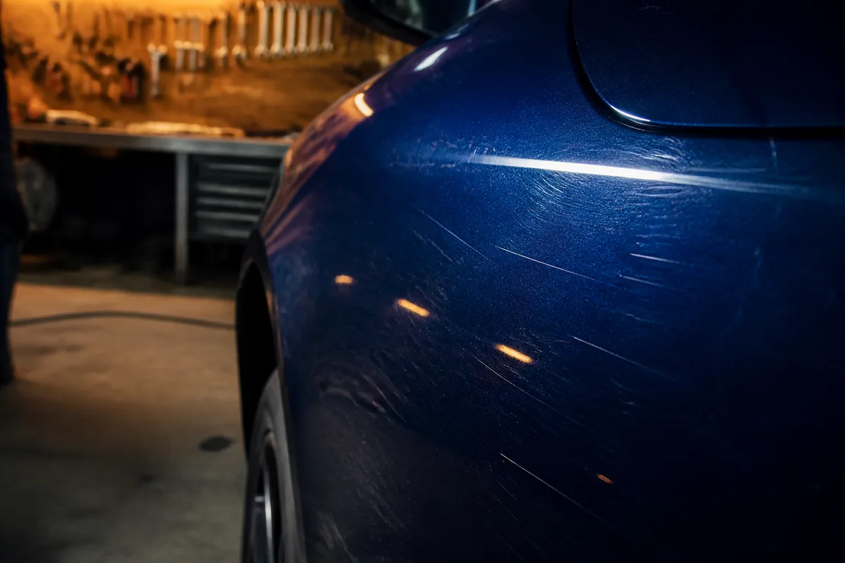 Vue rapprochée d&rsquo;une carrosserie bleue présentant plusieurs rayures superficielles sous une lumière rasante